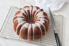 a bundt cake with white icing on a cooling rack next to a knife