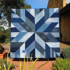 a blue and white quilt sitting on top of a wooden table next to some plants