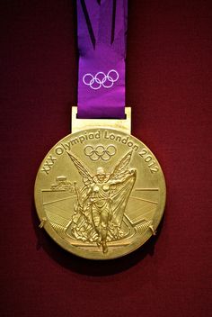 a gold medal with a purple ribbon around it and the olympic logo in the background