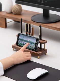 a person pointing at a cell phone on a desk with a mouse and keyboard next to it