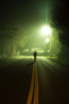 a person is walking down the road at night with a street light in the background