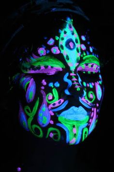 a woman's face painted with fluorescent colors in the dark, while she has her eyes closed