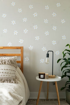 a bedroom with white flowers on the wall next to a bed and side table in front of it