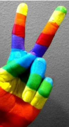 a person making a peace sign made out of rainbow colored paint on their hands and fingers