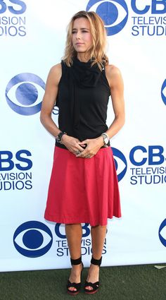 a woman in a black top and red skirt on the green carpet at an event