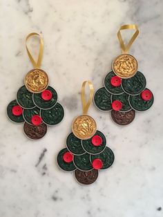 three christmas tree ornaments with red and green buttons on them, hanging from gold ribbon