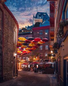 an alley way with many umbrellas hanging from the ceiling and buildings in the background