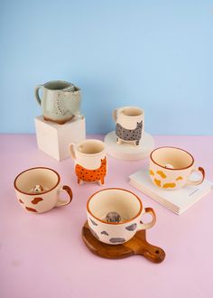 a table topped with cups and saucers on top of a pink surface