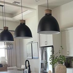 three lights hanging over a kitchen island in a home with white cabinets and stainless steel appliances