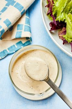 a bowl of dressing next to a plate of salad