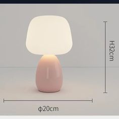 a white lamp sitting on top of a table next to a light pink base with a white shade