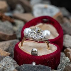 an engagement ring in a red velvet box with two pearls on the inside and outside