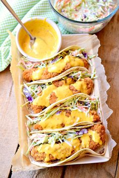 several tacos are lined up on a tray with dipping sauce in the bowl next to them