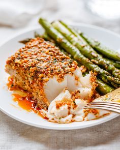 a white plate topped with fish and asparagus covered in seasoning next to a fork