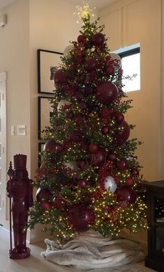 a christmas tree with red balls and lights in a living room next to a fire hydrant