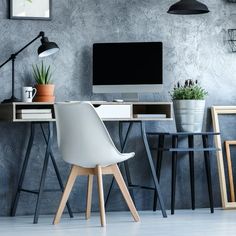 a desk with a computer, chair and potted plant on it in front of a gray wall