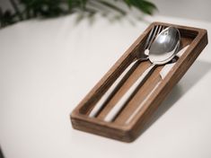 a fork and spoon in a wooden tray on a table with white cloth underneath it