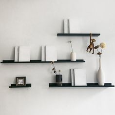 three black shelves with vases, books and other items on them against a white wall