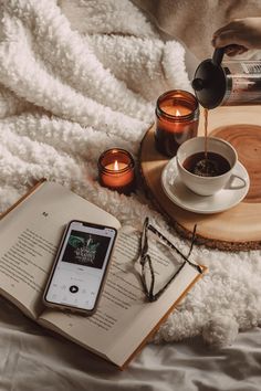 an open book and some glasses on top of a bed next to a cup of coffee