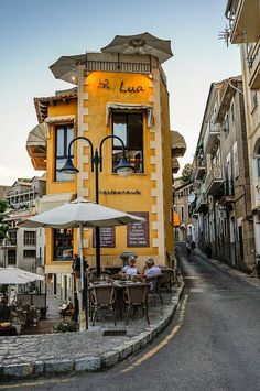 an outdoor cafe with tables and umbrellas on the side of the road in front of buildings