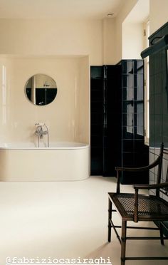 a white bath tub sitting next to a wooden chair in a bathroom under a round mirror