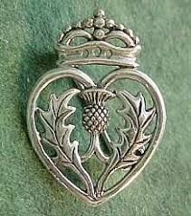 a heart shaped brooch with an ornate crown on the front and sides, sitting on a green surface