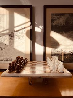 a chess board is on a table in front of two framed pictures and one has pine cones