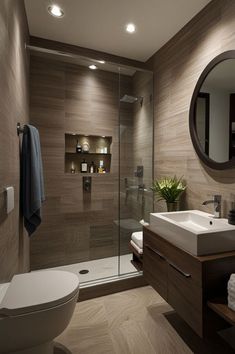 a bathroom with a toilet, sink and shower stall in the middle of it is illuminated by recessed lights