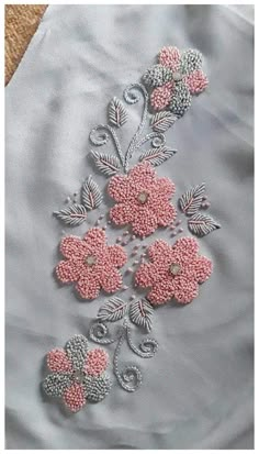 some pink flowers and leaves on a light blue shirt with silver thread work, in the shape of beads