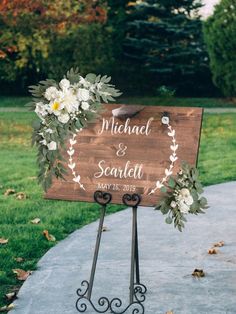 a wooden sign with white flowers and greenery on it