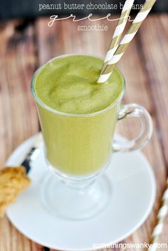 a green smoothie with two straws in it sitting on a white saucer