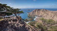 two people standing at the top of a mountain overlooking the ocean