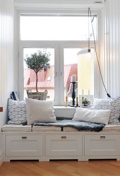 a window seat with pillows on it and a potted tree in the window sill