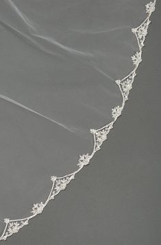 a white veil with flowers on it is hanging from the side of a gray wall