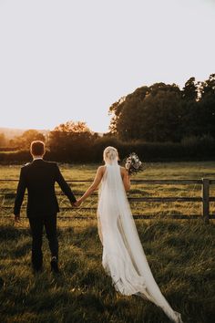 a bride and groom holding hands walking through the grass