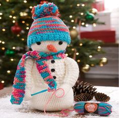 a crocheted snowman sitting next to a christmas tree