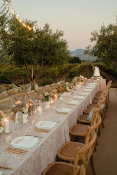 a long table is set up with white plates and place settings for an outdoor dinner