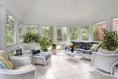 a sun room with white wicker furniture and large windows on the side of it