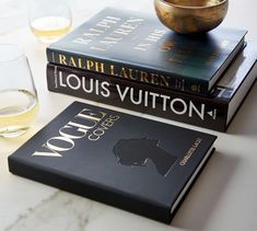 three books and two glasses sitting on a marble counter top next to each other,