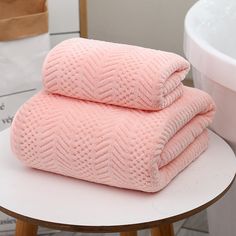 two folded pink towels sitting on top of a white table next to a bath tub