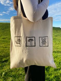 a woman holding a white bag with black drawings on it in front of a green field