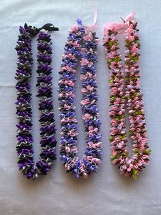 four necklaces are laid out on a white tablecloth with pink, purple and green flowers