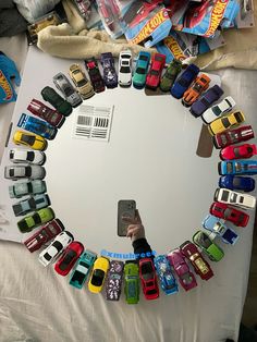 a person holding a cell phone in front of a circle of toy cars on a bed