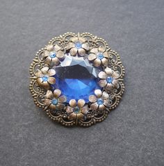 Czech style brooch, pressed filigree metal.  Large dark blue rhinestone in centre, flowers around the edge with smaller blue rhinestones. Pin and C clasp. Good condition. 5cm diameter. Czech Style, Vintage Brooch, Blue Rhinestones, The Edge, Vintage Brooches, Brooch Pin, Brooches, Dark Blue, Etsy Uk