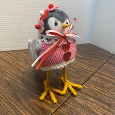 a small stuffed penguin wearing a pink dress and holding a red heart on its chest