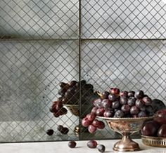 grapes and plums in a silver bowl on a marble counter top with a mirror behind them