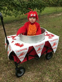 a child in a red costume sitting in a metal pail on top of grass