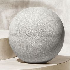 a large gray ball sitting on top of a cement block next to a white wall