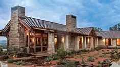 a stone and metal house with two chimneys on the roof, surrounded by greenery