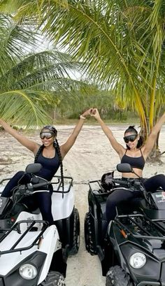 two women on four wheelers with palm trees in the backgroung and one holding her arms up